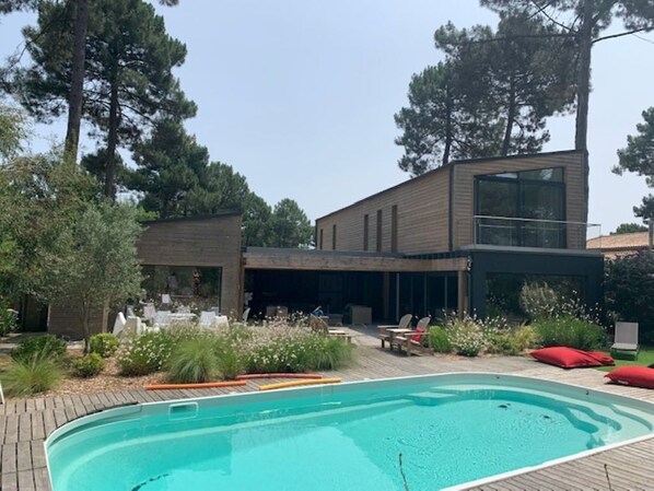 Ett modernt hus med en swimmingpool, utomhusmöbler och en trädgård.
