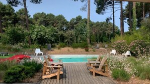 Una terrassa de fusta amb gandules, una piscina i un bosc al fons.