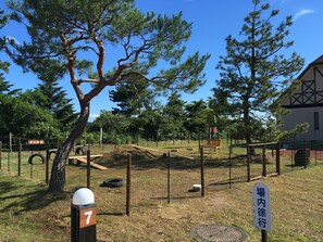 A fenced outdoor area with a wooden bench, a tree, and a sign with Japanese characters. - Heart Land Hills in Noto 35 Cabin A (Nanao)