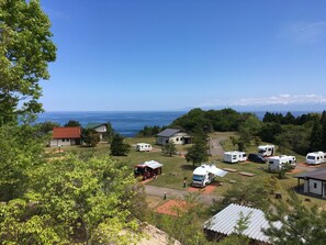 A campground with RVs and cabins, surrounded by trees and a view of the ocean. - Heart Land Hills in Noto 35 Cabin A (Nanao)
