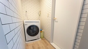 Pesuhuone, jossa on etuaukollinen pesukone, puulattia ja valkoisilla laatoilla päällystetyt seinät.