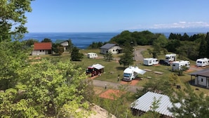 A campsite with RVs and mobile homes, a small building with a red roof, and a view of the ocean. - Heart Land Hills in Noto 38 Trailer House Chu (Nanao)