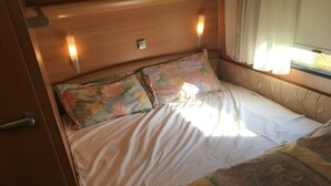 A bed with floral bedding and a patterned throw, a bedside table with a lamp, and a window with curtains. - Heart Land Hills in Noto 38 Trailer House Chu (Nanao)