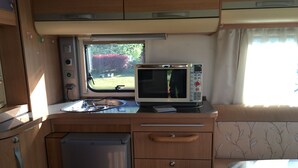 A compact kitchenette with a microwave, a small refrigerator, and a window providing a view of greenery outside. - Heart Land Hills in Noto 38 Trailer House Chu (Nanao)