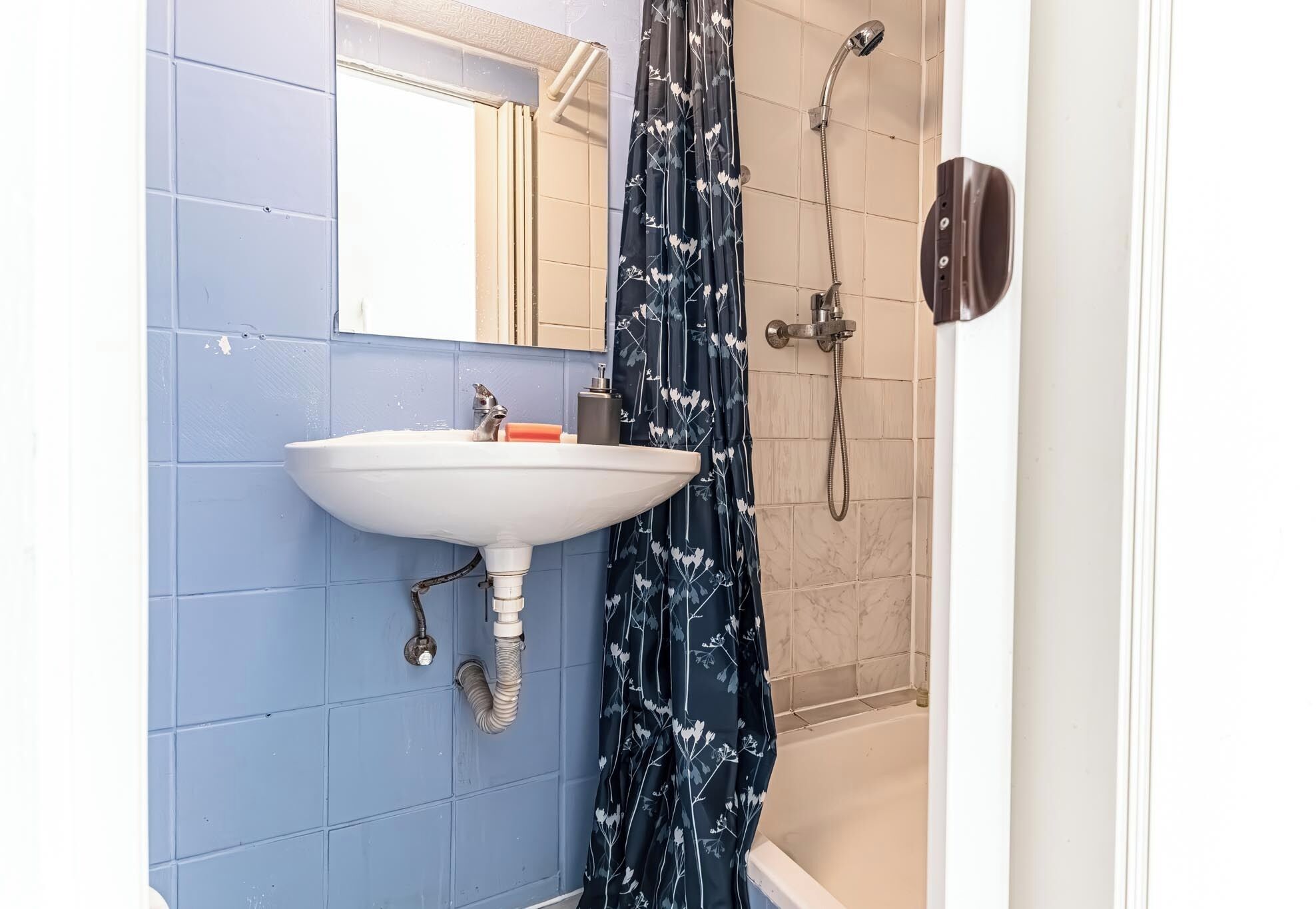 Une salle de bain équipée d’un lavabo, d’un miroir, d’une douche et d’une porte avec une poignée.