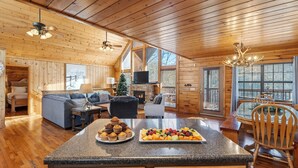 Un intérieur de chalet chaleureux, avec un revêtement mural en bois, une cheminée, un coin repas et une cuisine dotée d’un comptoir en granit.