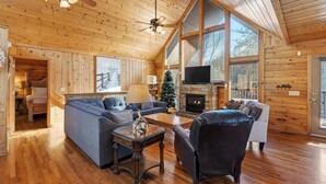 L’intérieur d’un chalet accueillant, avec un plafond en bois, une cheminée, un canapé, un fauteuil et un téléviseur.