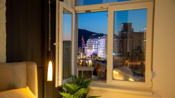 A room with a view of a cityscape at dusk, a window, and a plant. - Stone Bridge Apartment (Skopje)