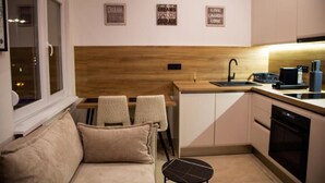 A compact kitchen with a wooden countertop, a sink, and a dishwasher. There are two chairs and a small table. - Stone Bridge Apartment (Skopje)