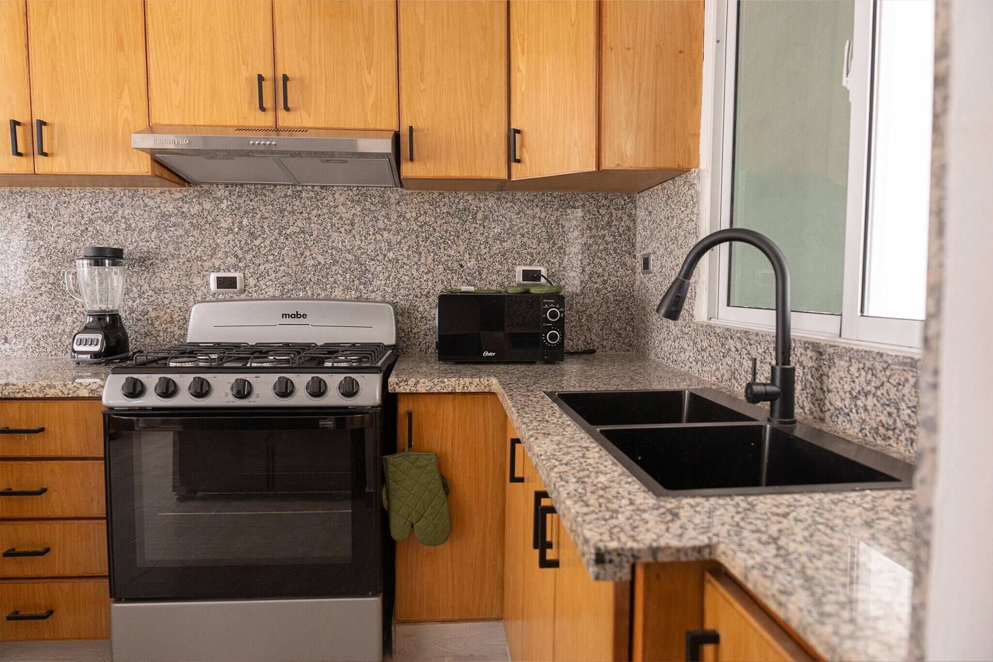 Une cuisine avec des meubles de rangement en bois, une cuisinière, un four à micro-ondes, un évier et une fenêtre.