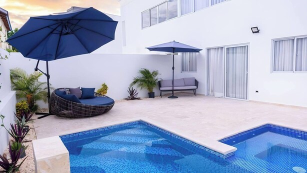 Ein Swimmingpool mit Liegestuhl und einer Sitzecke mit Sonnenschirmen.