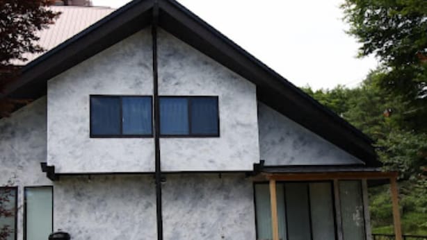 Una casa de dos pisos con fachada simétrica, ventanas grandes y una terraza de madera.