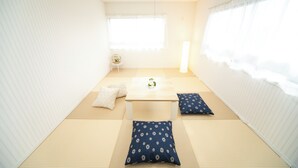 Een traditionele Japanse kamer met tatami vloerbedekking, een lage tafel met kussens en een raam met transparante gordijnen.