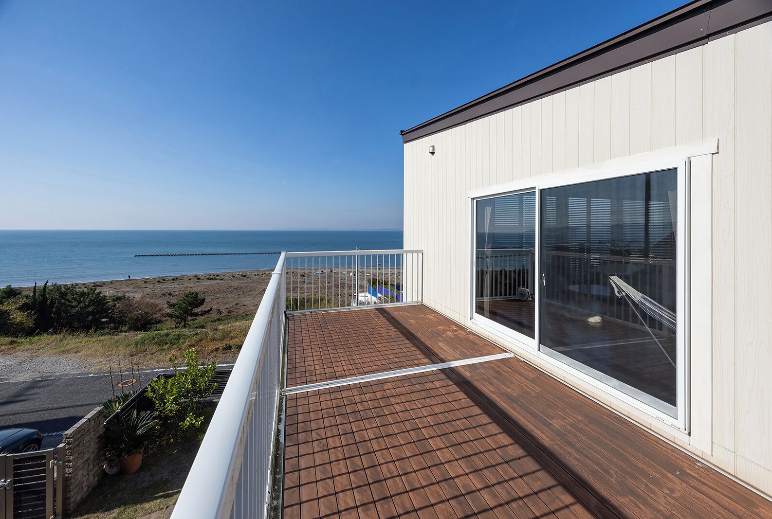 Un balcon avec vue sur la mer, un bâtiment blanc et une terrasse en bois.