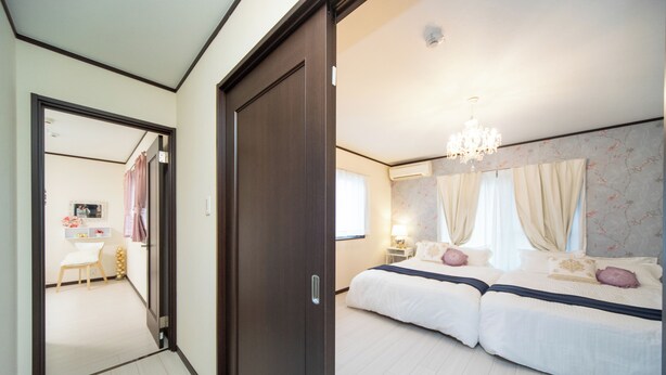 A bedroom with two beds, a chandelier, and a bathroom visible through an open door. - Awaji Central in Kuruma (Awaji)