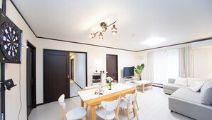 A modern living room with a dining area, a grey sofa, a flat-screen TV, and a dartboard on the wall. - Awaji Central in Kuruma (Awaji)