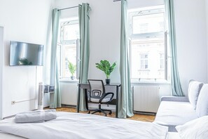 A modern hotel room with a bed, a desk with a chair, a potted plant, and a TV on the wall. - Bright Modern Apt Danube Canal Area (Vienna)