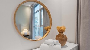 Un baño con un espejo redondo, un florero con flores secas y toallas dobladas con cuidado sobre un tocador blanco.