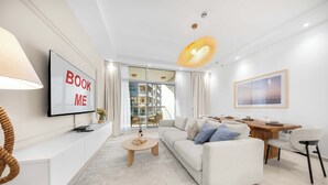 Una sala moderna con sofá, mesa de centro, televisor y comedor con mesa y sillas de madera.