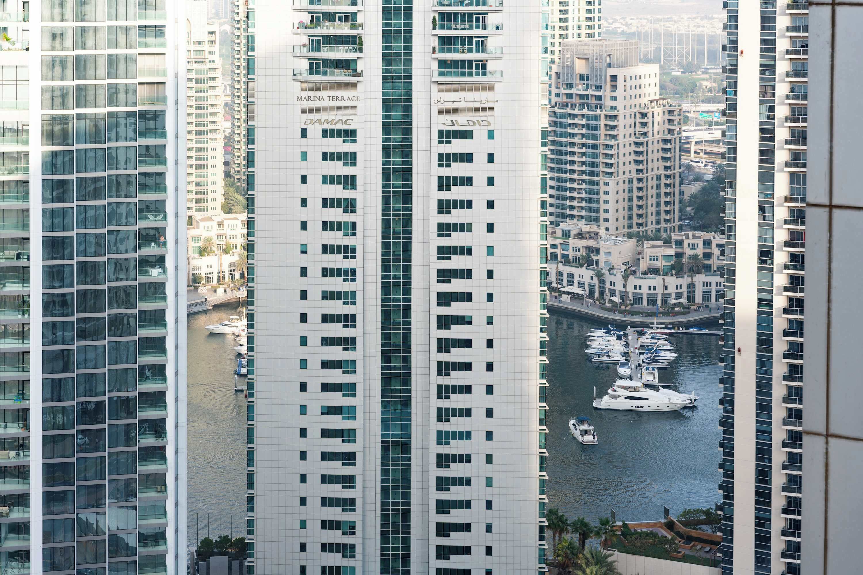 A high-rise building with multiple balconies, a marina with yachts, and a view of the marina.