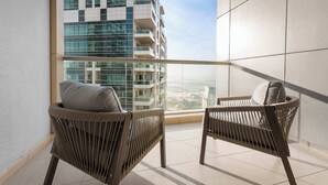 Un balcón con dos sillones de mimbre y vistas a un edificio moderno.