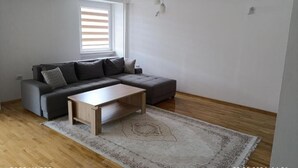 Ein modernes Wohnzimmer mit einem grauen Ecksofa, einem Holztisch und einem gemusterten Teppich.
