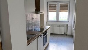 Eine Küche mit weißen Schränken, einem Herd und einem Fenster mit Jalousien.