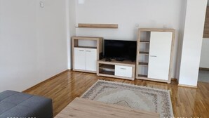Ein modernes Wohnzimmer mit einem Flachbildfernseher, Holzschränken und einem grauen Sofa.