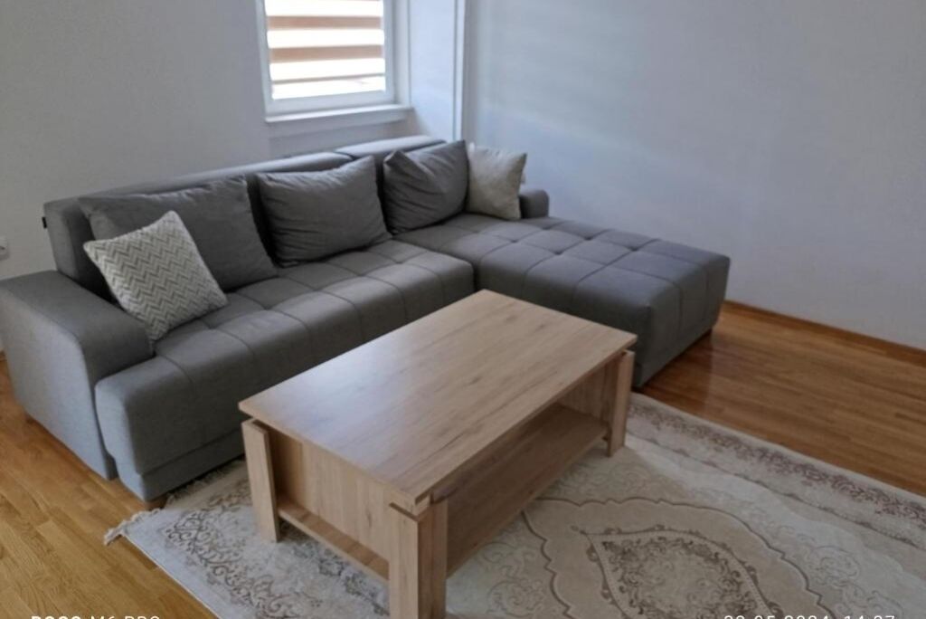 Ein modernes Wohnzimmer mit einem grauen Ecksofa, einem Holztisch und einem gemusterten Teppich.