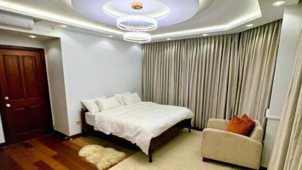 A bedroom with a bed, a chair, a wooden floor, a white rug, and a ceiling light fixture. - Luxury Sea View 3 Bedroom AC Apartment 5 star hotel access and all amenities (Colombo)