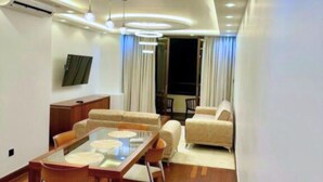 A modern living room with a glass dining table, sofas, and a TV mounted on the wall. - Luxury Sea View 3 Bedroom AC Apartment 5 star hotel access and all amenities (Colombo)