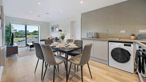 Cozinha moderna com máquina de lavar embutida, área de jantar com mesa posta para quatro pessoas e vista para o exterior.