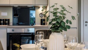 Uma cozinha moderna com eletrodomésticos de aço inoxidável, uma área de refeições com louças brancas e um vaso de plantas.