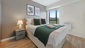 Quarto moderno com uma cama grande, mesa de cabeceira com abajur e janela com vista para a cidade.