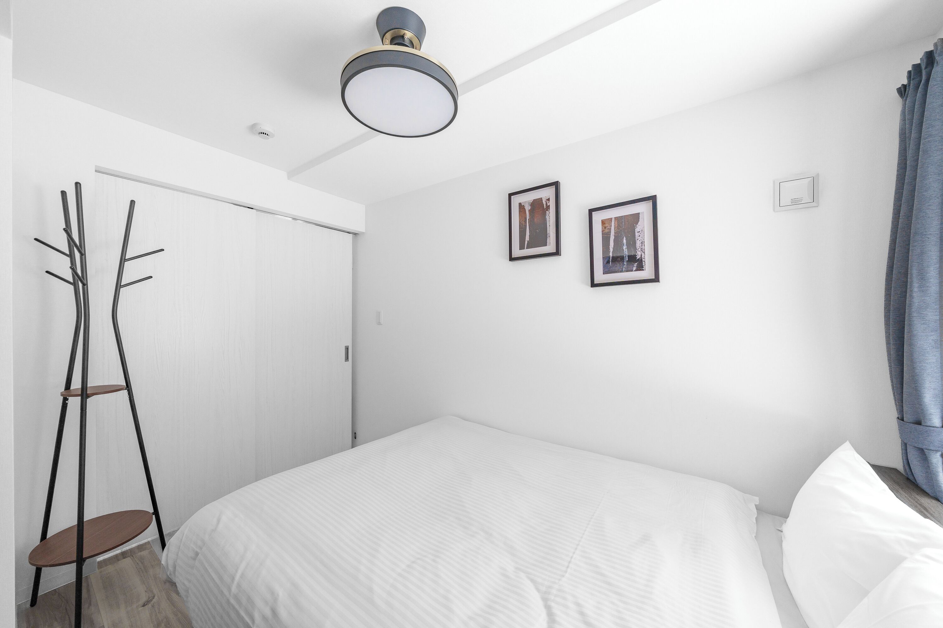 A minimalist bedroom with a bed, a coat rack, and two framed pictures on the wall.