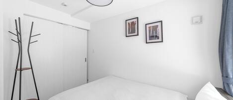 A minimalist bedroom with a bed, a coat rack, and two framed pictures on the wall.