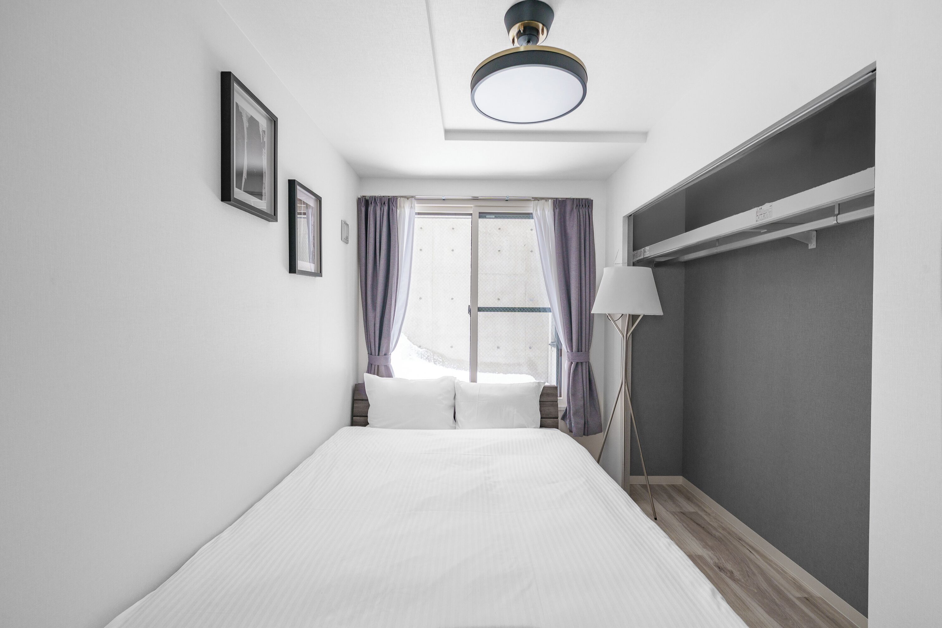 Een moderne hotelkamer met een bed, een raam met gordijnen, een bedlamp en een kledingkast.