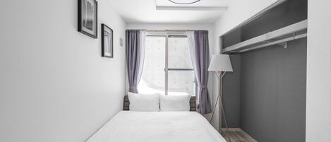 Een moderne hotelkamer met een bed, een raam met gordijnen, een bedlamp en een kledingkast.
