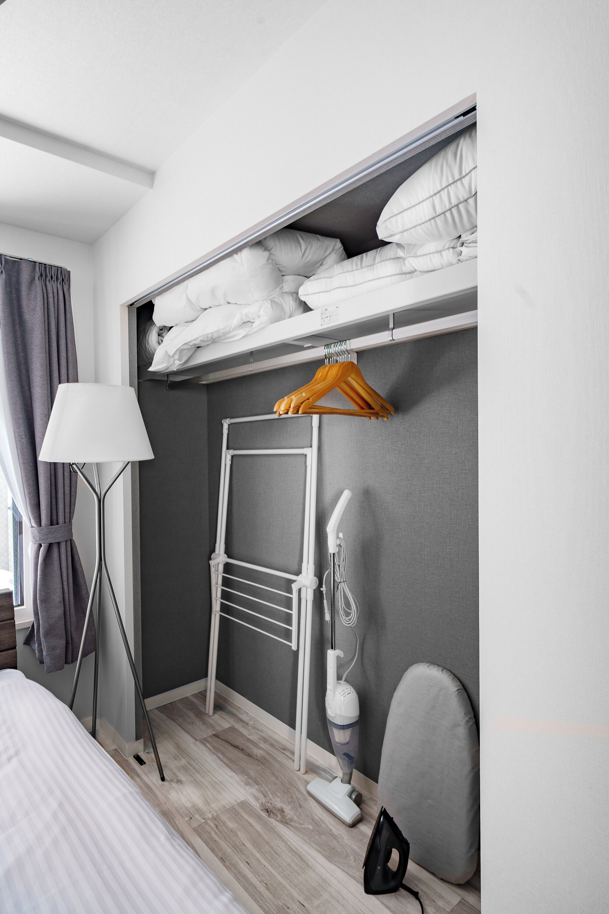 A compact hotel room with a bunk bed, a bedside table, a lamp, a vacuum cleaner, and a chair.