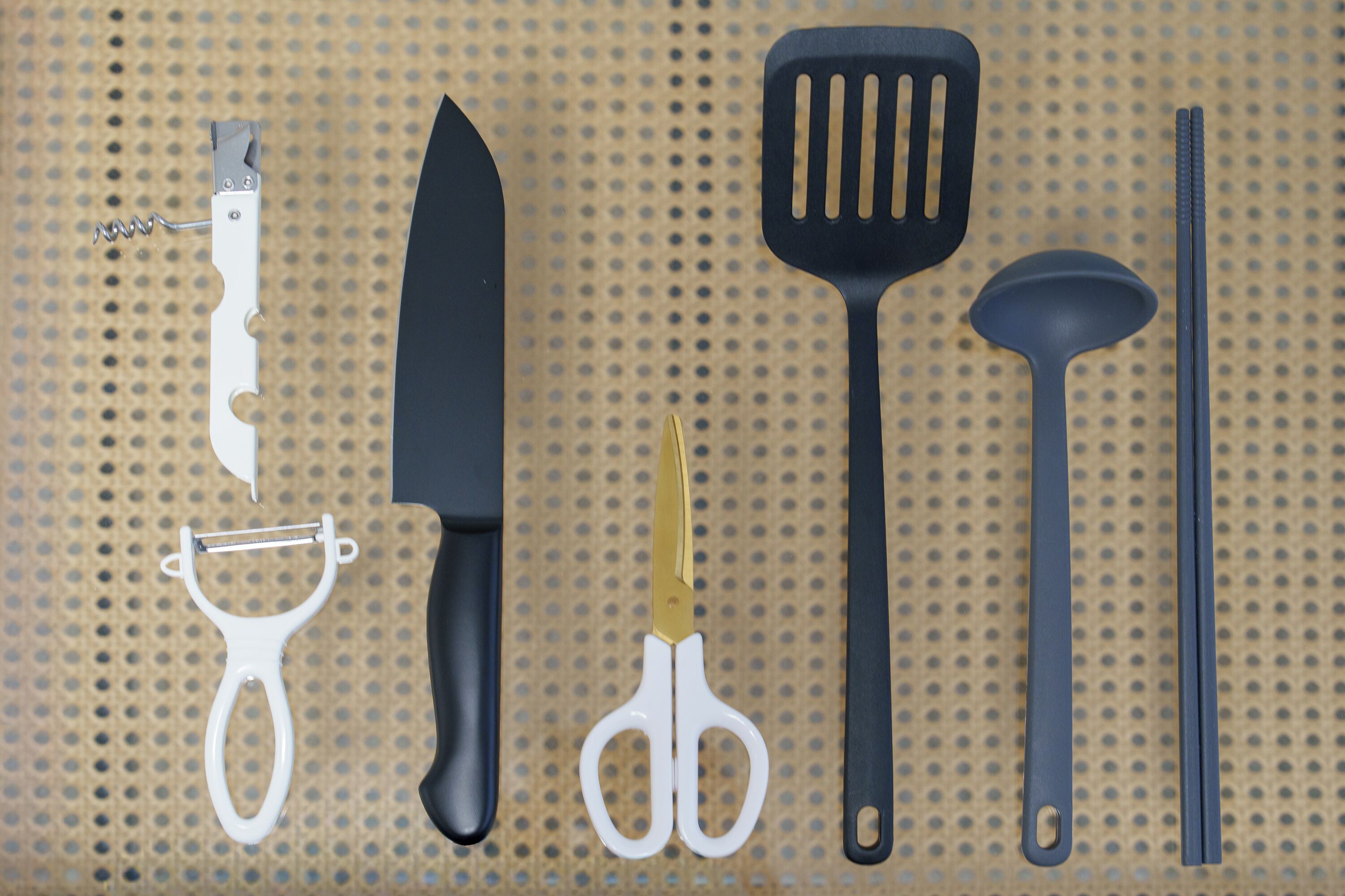Diversi utensili da cucina, tra cui un coltello, forbici e una grattugia, disposti su una superficie forata.