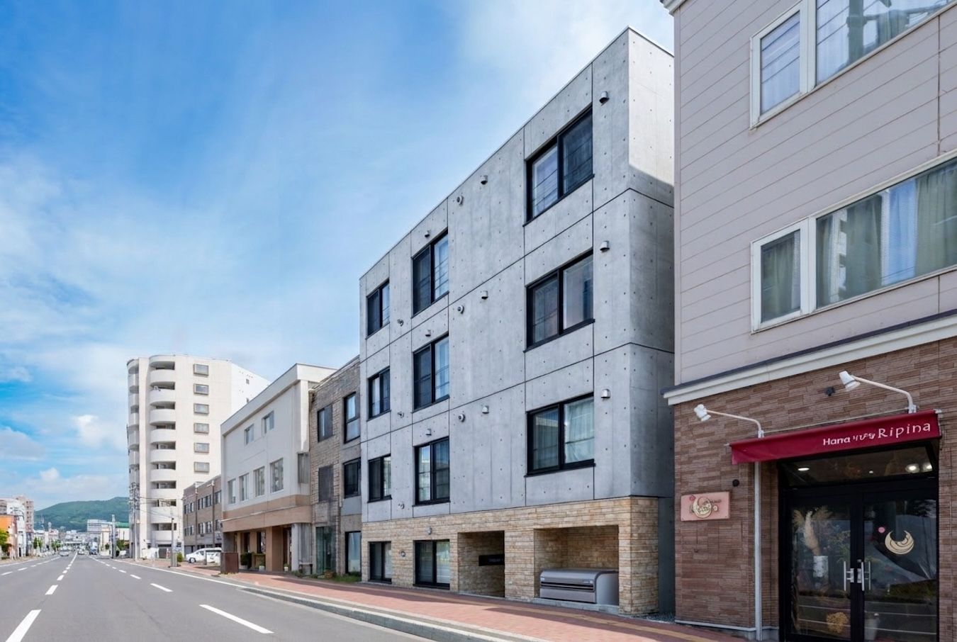 Een modern meerijverig gebouw met een vlakke gevel, grote ramen en een zichtbaar restaurant genaamd 'Hana no Ripina' op de begane grond.