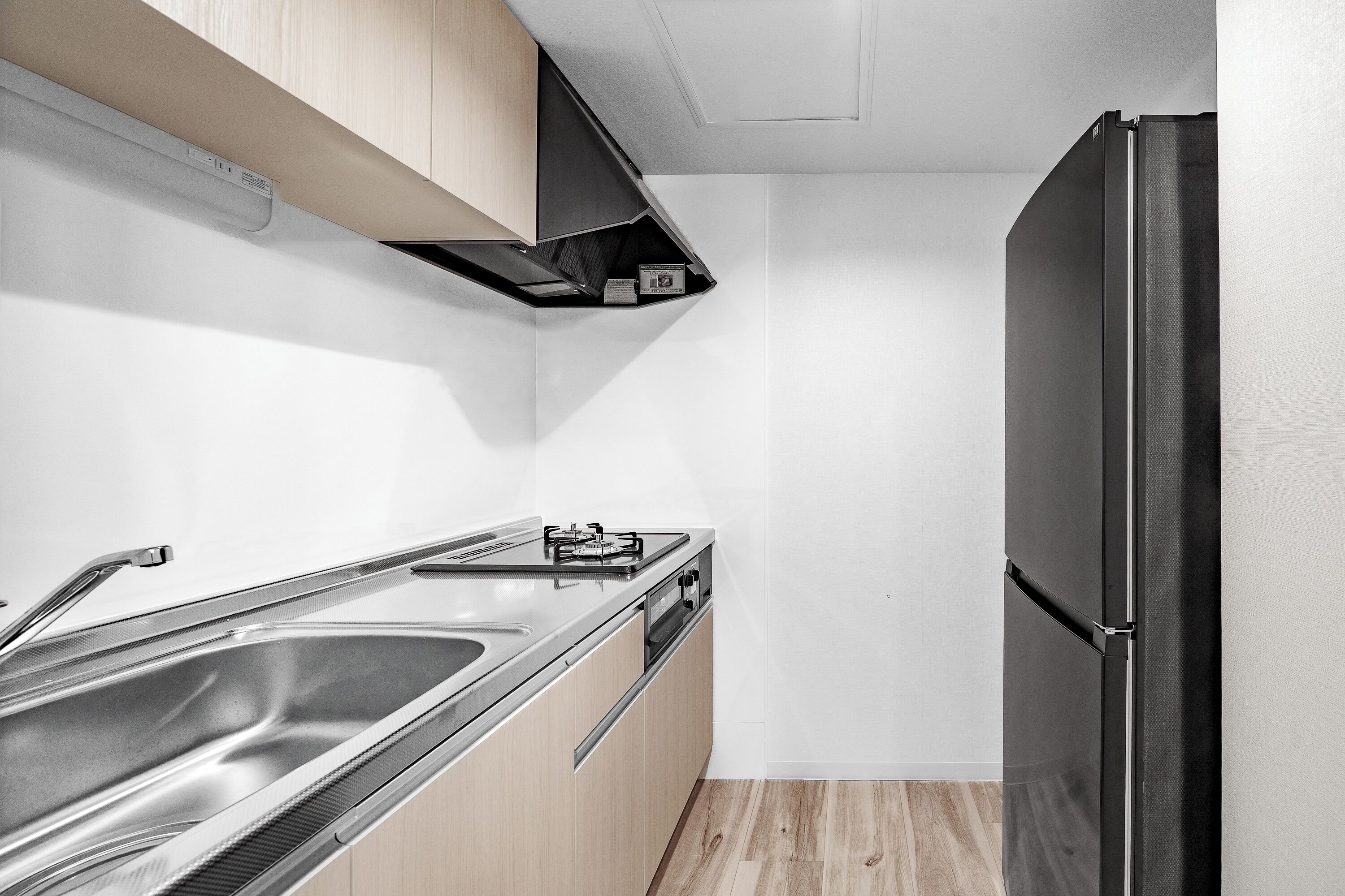 A compact kitchen with a black refrigerator, stainless steel sink, and wooden cabinets.