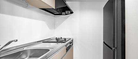 A compact kitchen with a black refrigerator, stainless steel sink, and wooden cabinets.