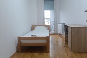 Une petite chambre avec un lit simple, un radiateur et une armoire en bois.
