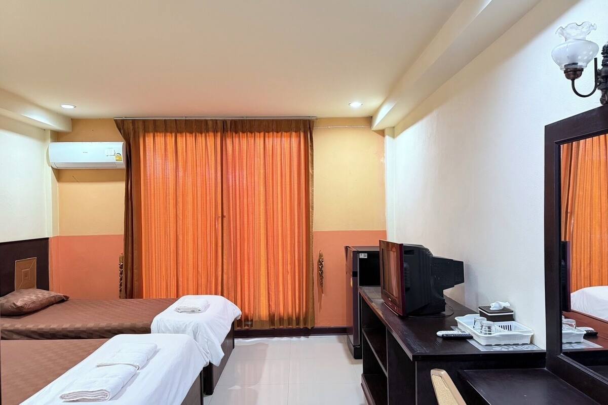 A hotel room with two beds, a TV, a desk with a mirror, and an air conditioning unit.