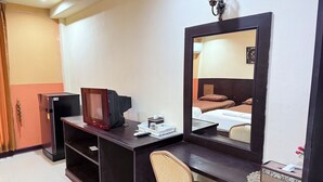 A hotel room with a dark wooden desk, a chair, a television, a mirror, and a bed with two pillows.