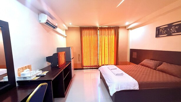 A hotel room with a bed, desk, and an air conditioning unit.