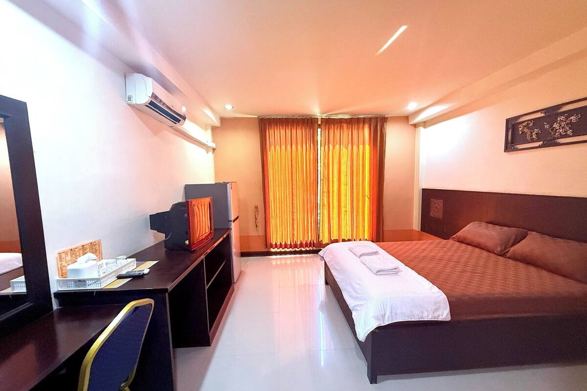 A hotel room with a bed, desk, and an air conditioning unit.