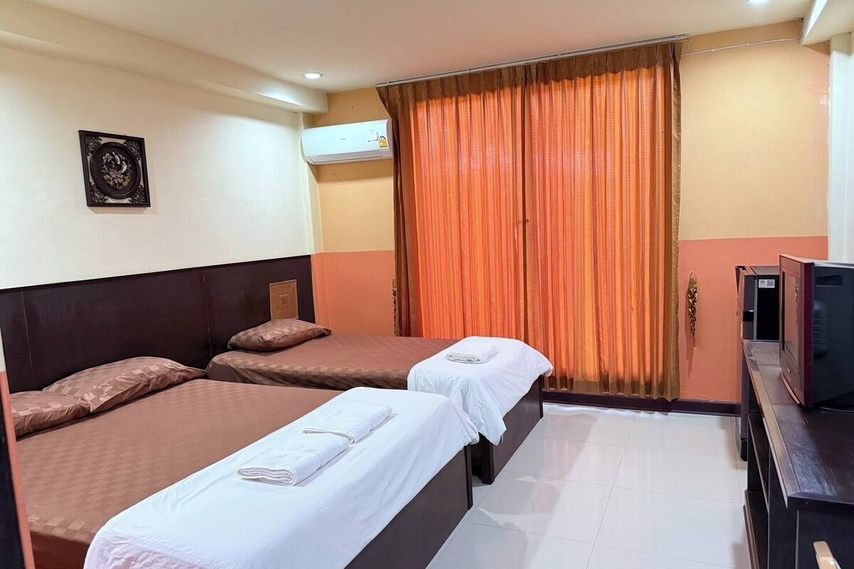 A hotel room with two beds, a TV, and an air conditioning unit.