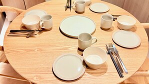 Pyöreä puinen ruokapöytä, jonka päällä on lautasia, kulhoja ja ruokailuvälineitä.